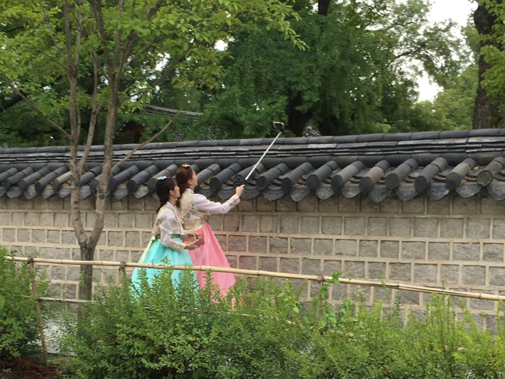 Two young women in traditional costume visit the traditional Hanok Village in Jeonju, South Korea, and take selfies with a selfie stick